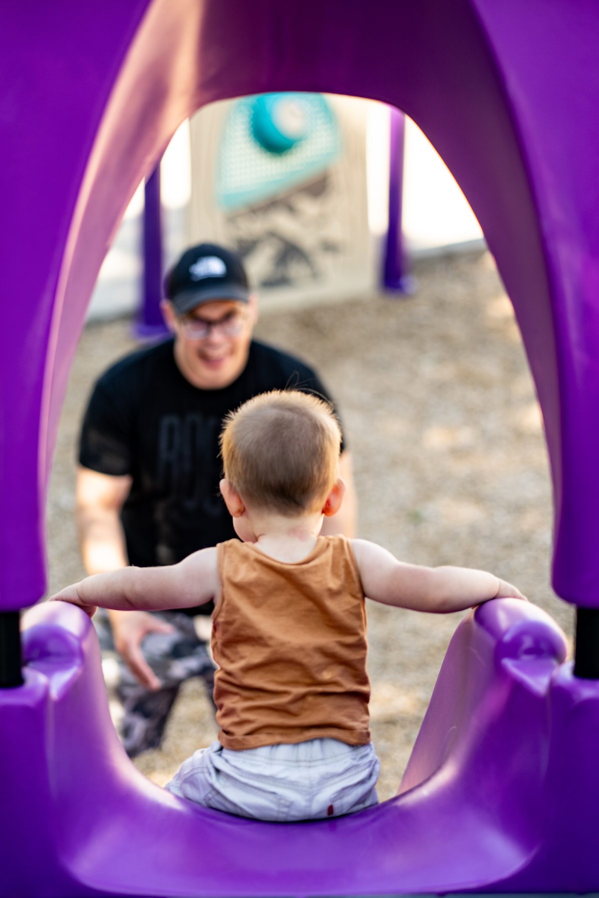 Toddler at the top of a purple playground tunnel with an adult waiting below