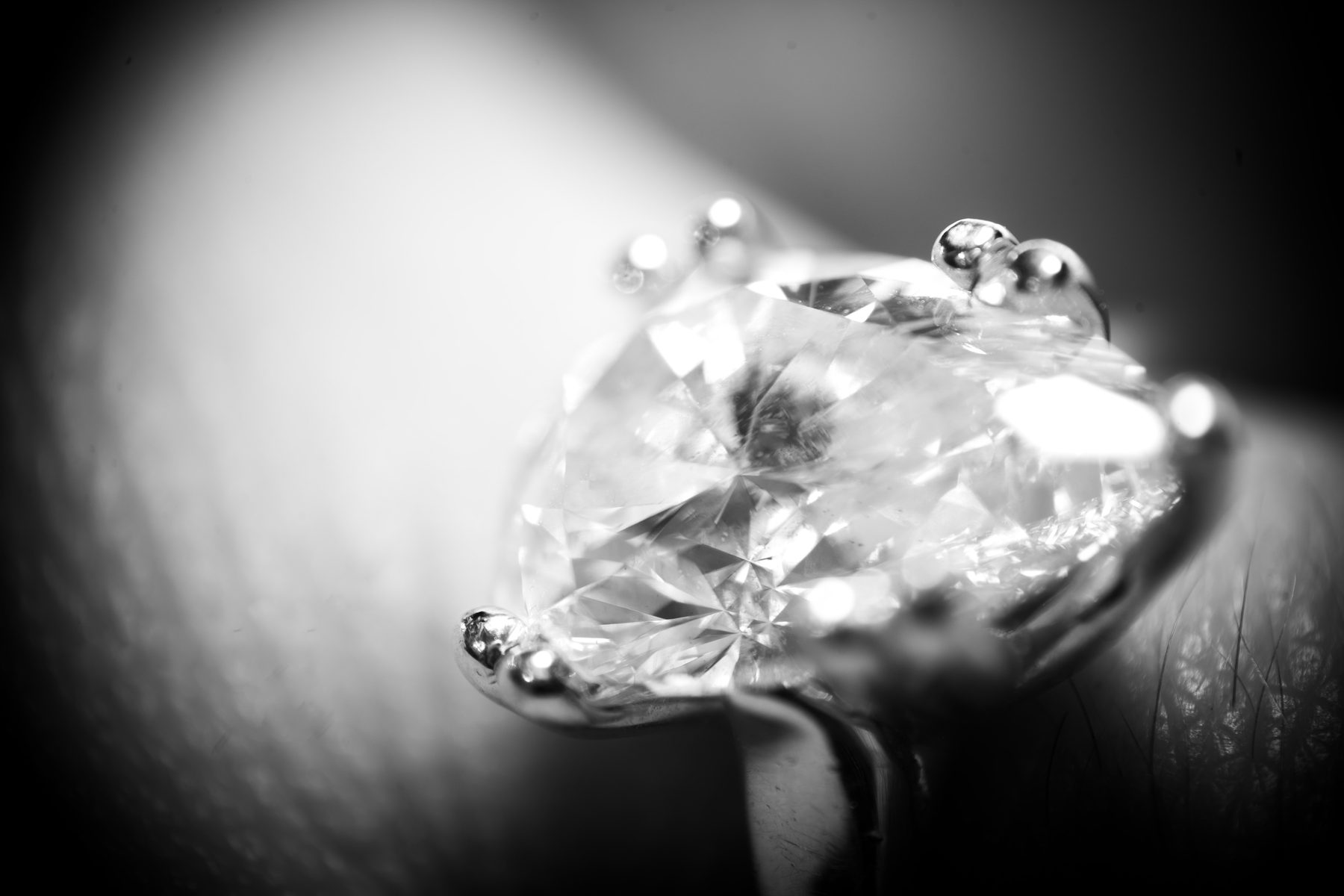 Black-and-white close-up of a clear faceted gemstone and polished ring prongs