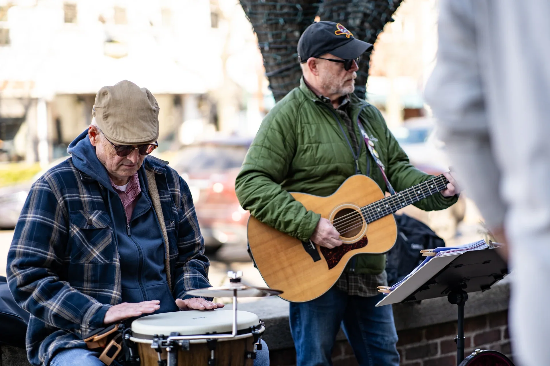 Two street musicians playing guitar and hand drums outdoors