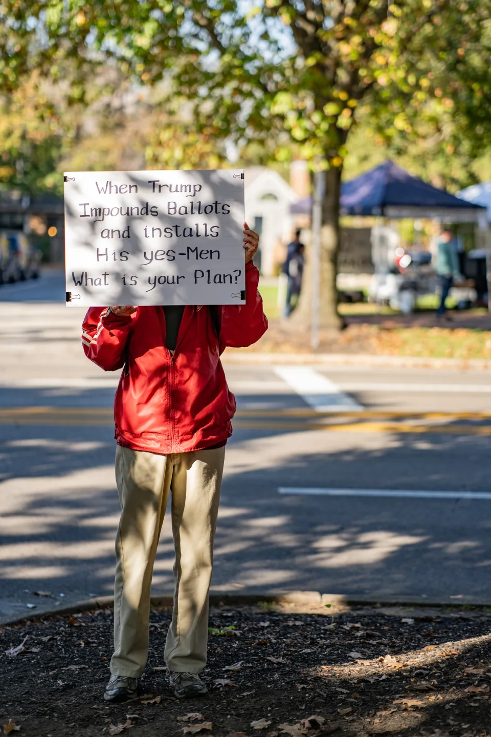 A person holding a handwritten sign beneath autumn trees