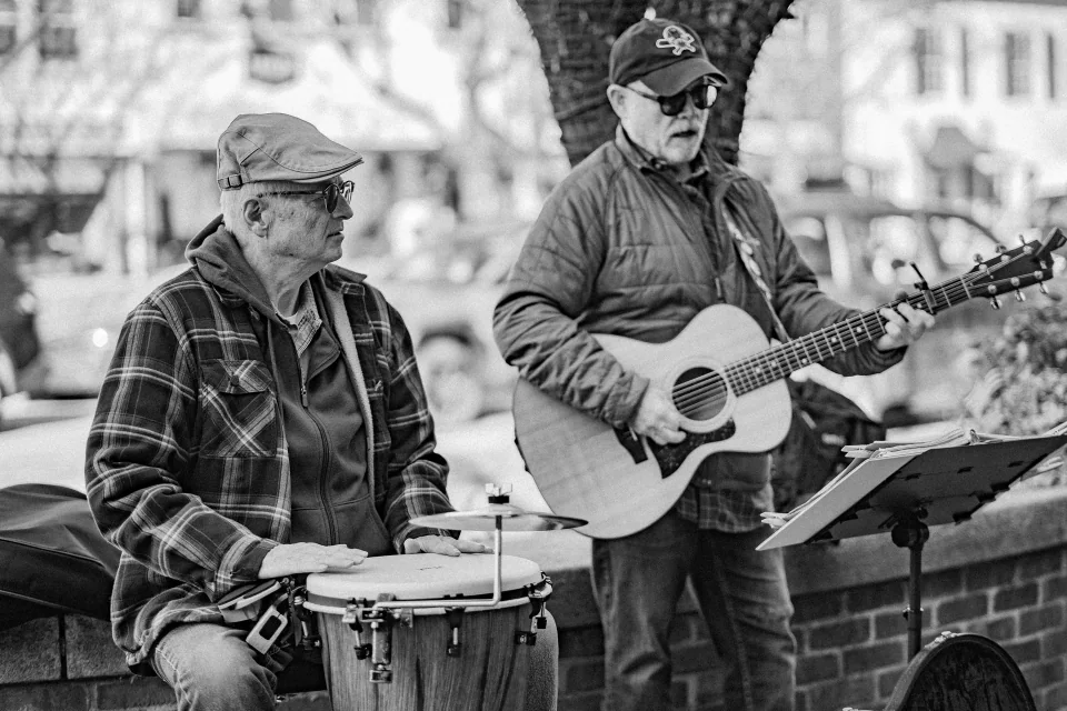 Two street musicians playing guitar and hand drums, in black and white