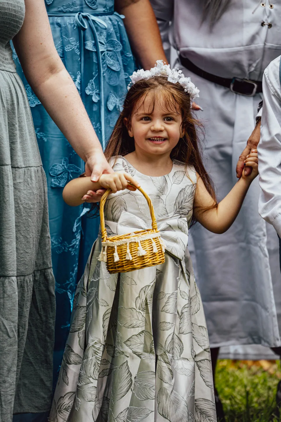 A small child holding a basket while standing among adults at a wedding