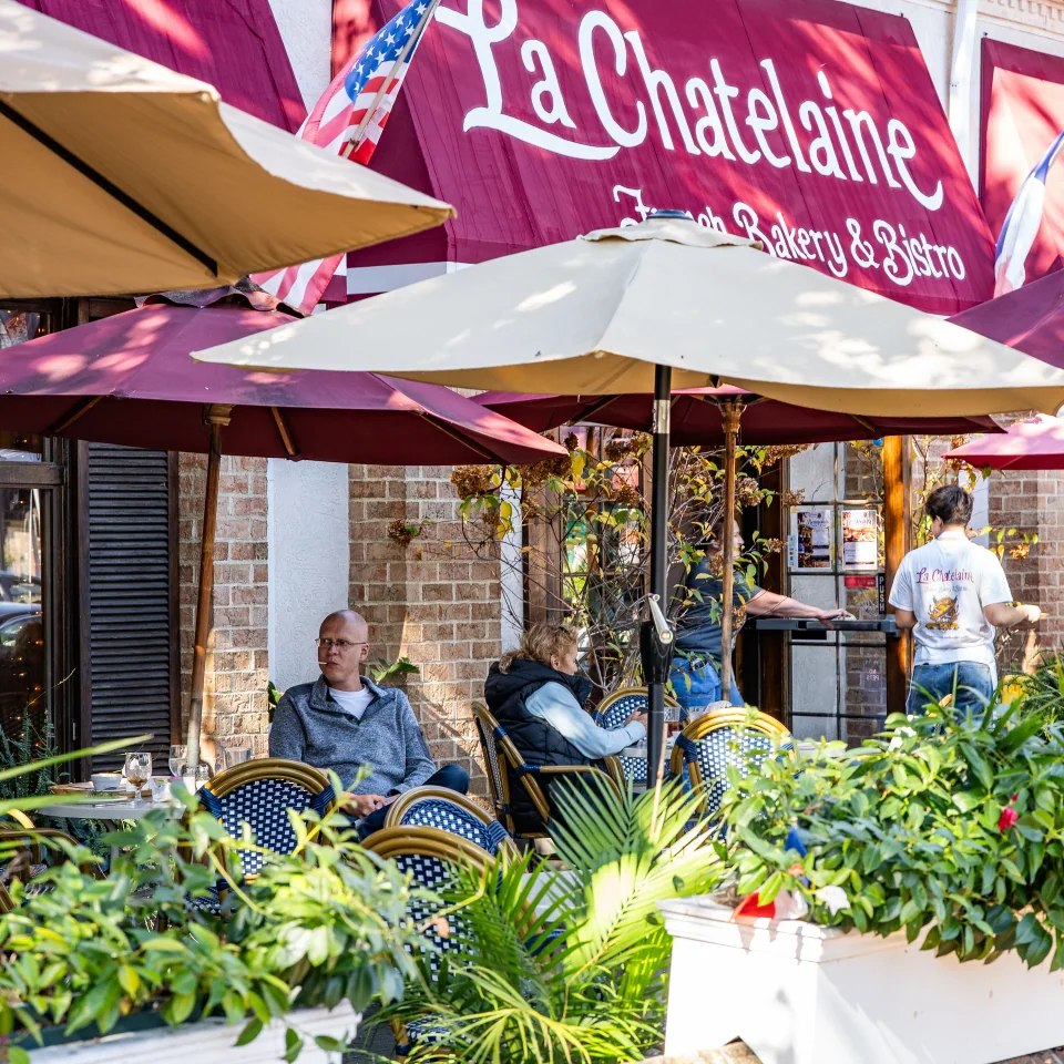 People seated outside a cafe beneath colorful umbrellas and a La Chatelaine sign