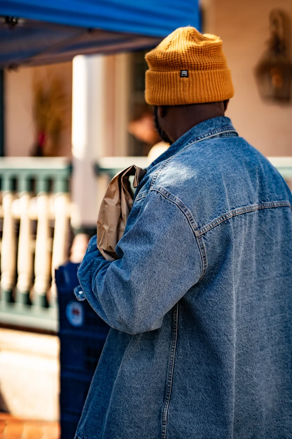 A person in a denim jacket and yellow hat beside a brick wall
