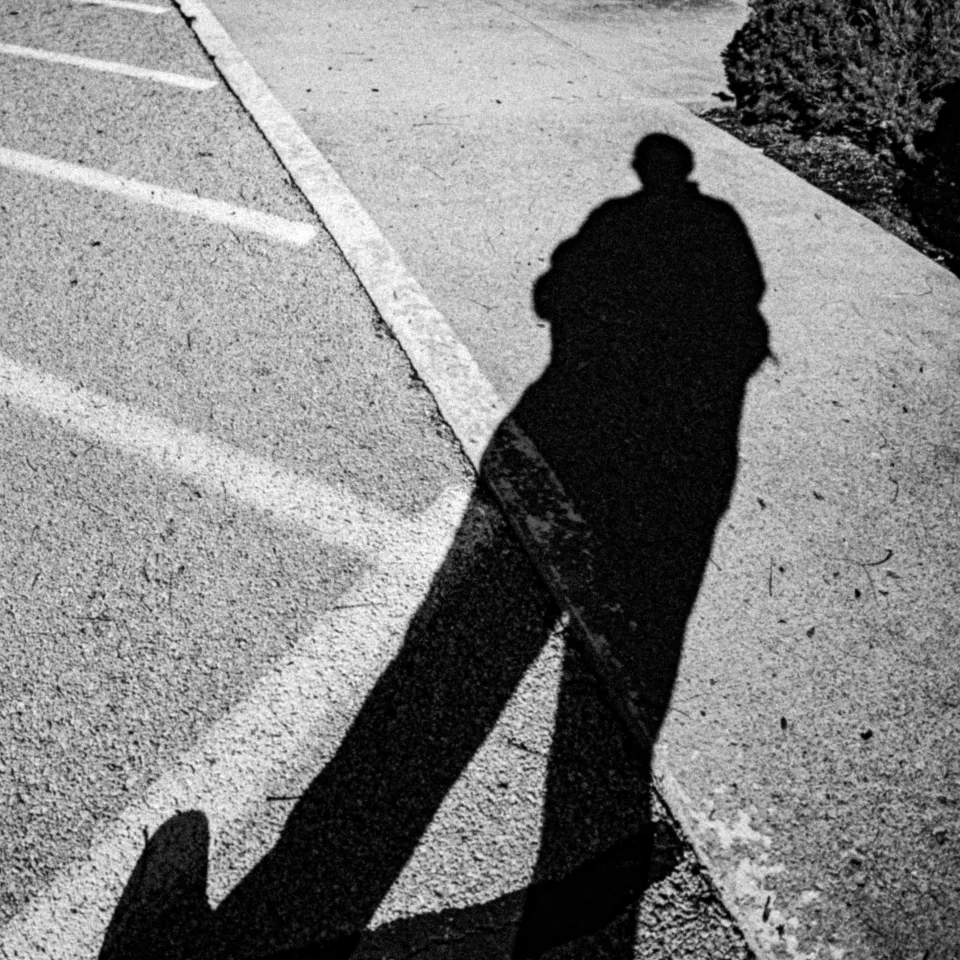 A long human shadow across a painted line on the pavement, in black and white