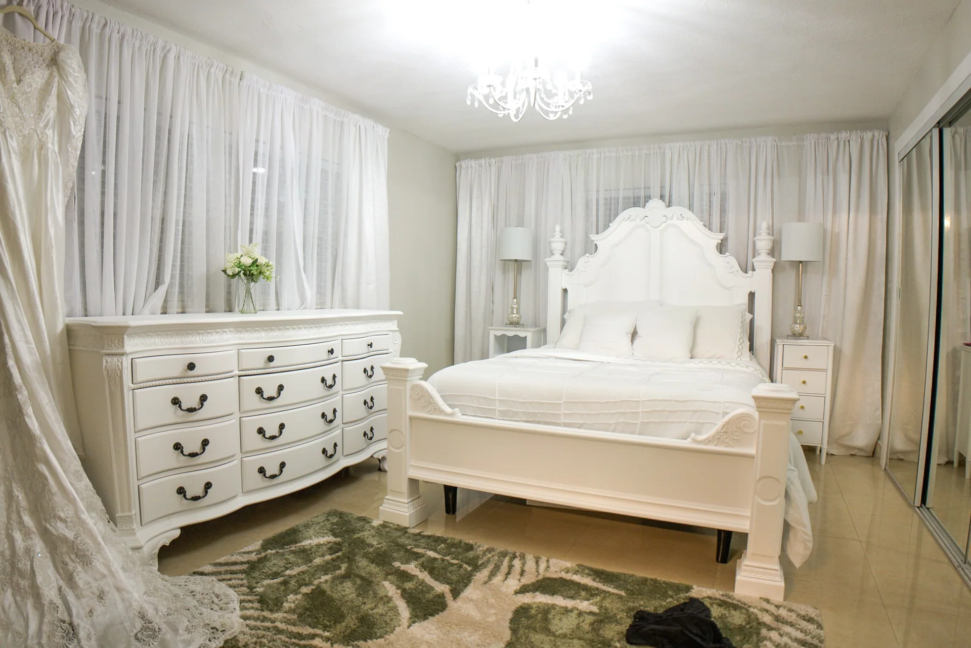 Bright white bedroom with ornate furnishings and a wall of windows