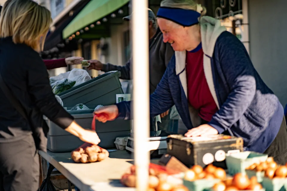 A vendor handing a small item across an outdoor market table